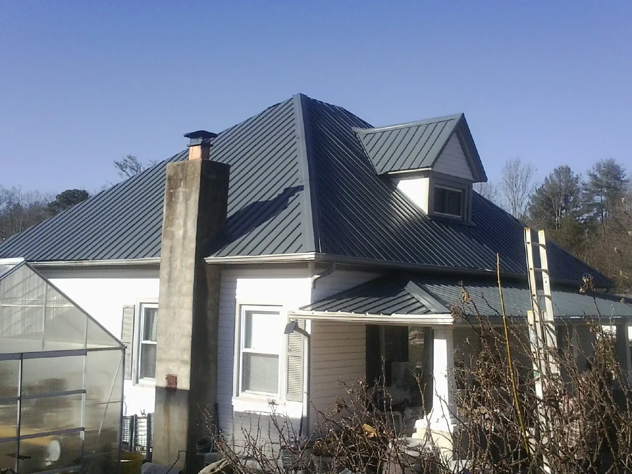 Dark blue standing seam metal roof on a white farmhouse with dormer — Slate & Tile Roof Repair by Roofing Brothers in Sylvia
