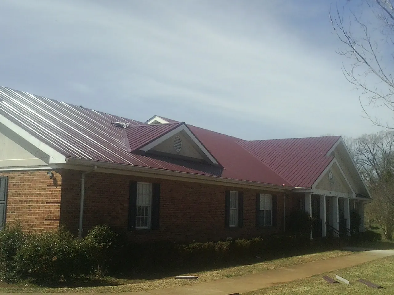 Red metal roof with gabled entries on a long brick building, from a Hail Damage Roof Repair job in Sylvia