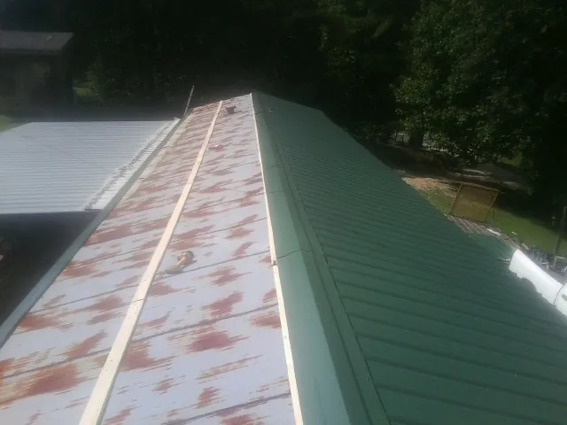 Old rusted panels beside newly installed green metal roofing — Wind Damage Roof Repair by Roofing Brothers in Sylvia