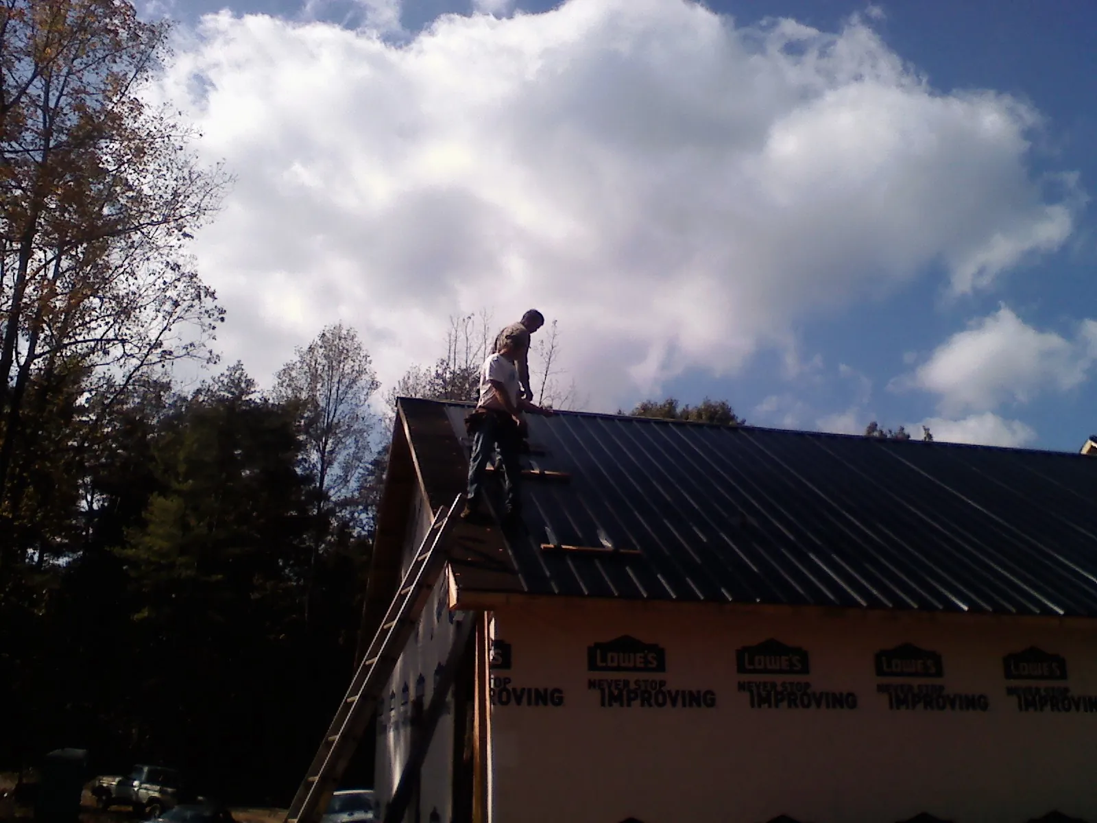 Roofer fastening dark metal panels high against a cloudy sky, from a Roof Inspection job in Sylvia