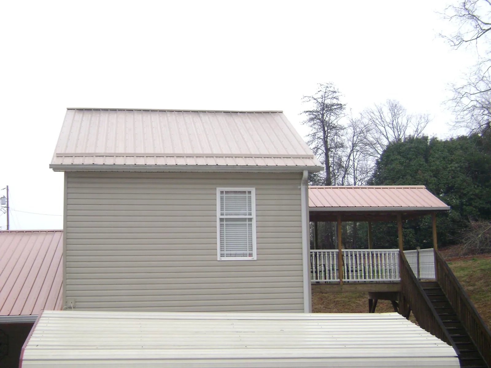 Tan metal roofs on a two story addition and attached porch, from a Roof Replacement job in Sylvia